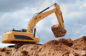 An excavator on a dirt mound lifting dirt.
